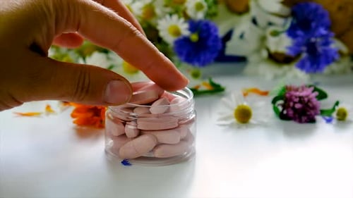 Hand Taking a Pill from Jar With Flowers