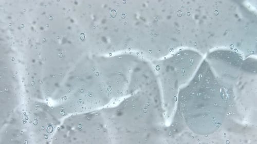 Transparent Blue Cosmetic Gel Fluid with Bubbles Flowing Down on a White Surface