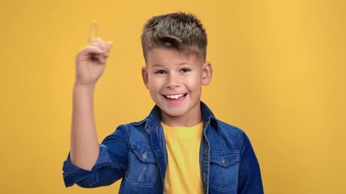 Excited Boy Points Upwards on Yellow Background