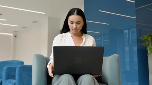 Woman Typing on Laptop in Modern Office Lobby