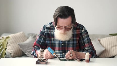 Man Soldering Circuit Board at Table Indoors