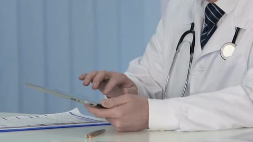 Médecin professionnel insérant des données à partir d'un document papier sur un Tablet PC moderne