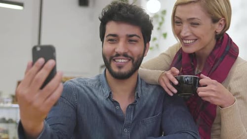 Happy couple with phone making video call in cafe