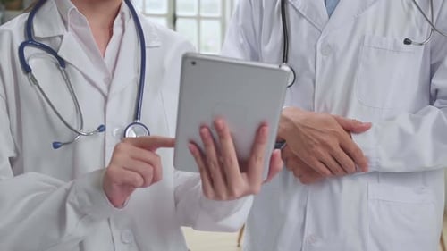 Doctor's Office: Asian Physician Talks With Professional Nurse, Using Tablet Computer