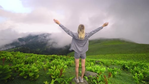 Woman Raises Arms in the Air on Green Hillside