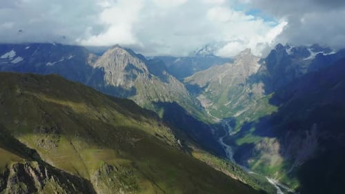 Aerial View of Snowcapped Mountain Peaks Covered By Clouds and Blue Sky on a Summer Day