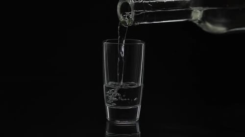 Pouring Up Shot of Vodka From a Bottle Into Glass. Black Background