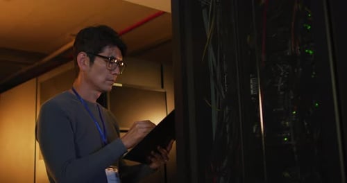 IT Professional Inspecting Servers with Tablet in Data Center