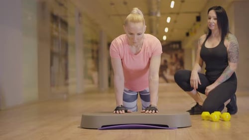 Professional Personal Trainer Controls Workout of Athletic Woman in Gym. Tattooed Caucasian Woman