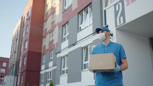 An Young Mailman Courier with a Protective Mask and Gloves is Delivering a Parcel Directly to a