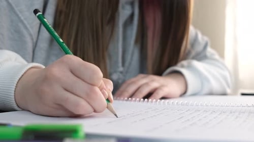 Student Writing in Notebook with Green Pencil