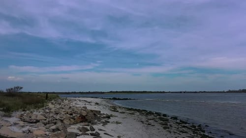 A low angle drone shot of an empty beach on a sunny day. The camera dolly out slowly over the rocky