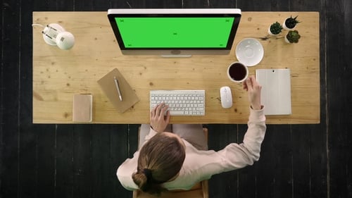 Woman Working at Desk with Green Screen Computer