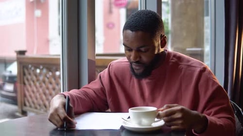 Young Adult Man Writing at Cafe with Coffee