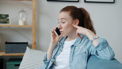 Cheerful Young Redhead Woman Speaking on Mobile Phone and Smiling Indoors in Apartment