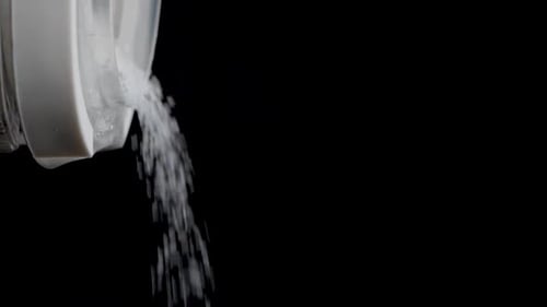 Close up shot of pouring out sugar out of a transparent container in slow motion.