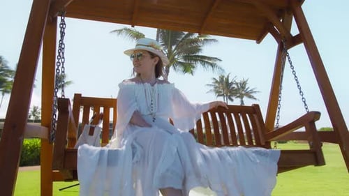 Woman Relaxes on Swing Under Tropical Palm Trees
