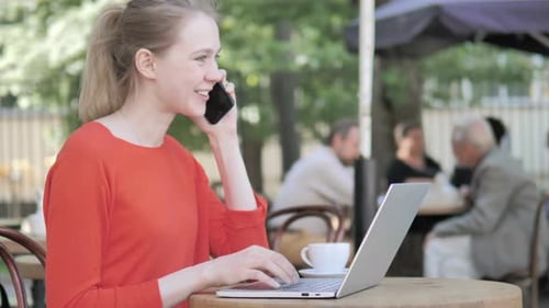 Young Woman Talking on Phone while Sitting in Cafe Terrace