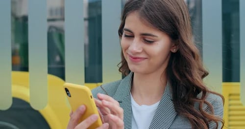 Close Up View of Millennial Woman Touching and Looking at Smartphone Screen at City Street. Happy