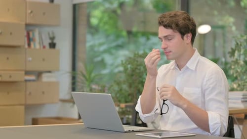 Young Man Having Headache While Working on Laptop in Modern Office