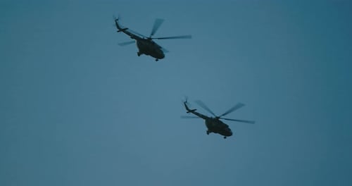 Two Army Helicopters Flying Across Blue Sky