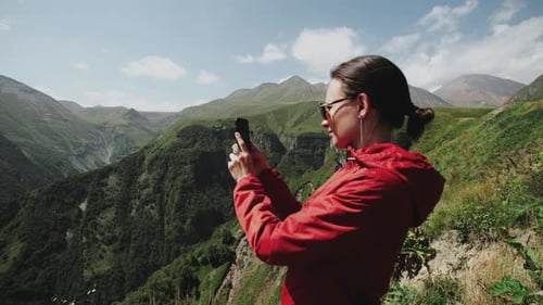 Woman Travel on the Edge of Cliff Over Mountain Gorge. Makes Photo of Alpine Landscape on Smartphone