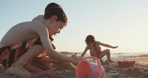 Three kids playing on the beach building sand castles together