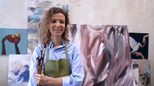 Smiling Artist Holding Brushes in Art Studio