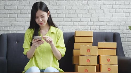 Young Woman with Mobile Phone Next to Shipping Boxes