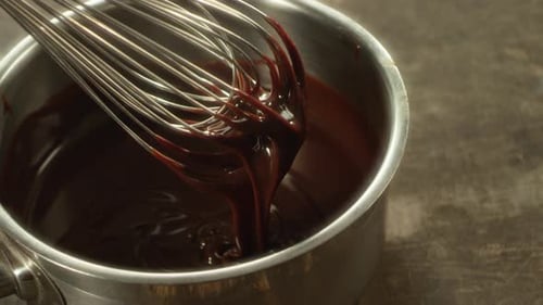 Nahaufnahme: Schlagen Sie flüssige Schokolade mit Metall-Schneebesen. Makro von Chocolate Stream.