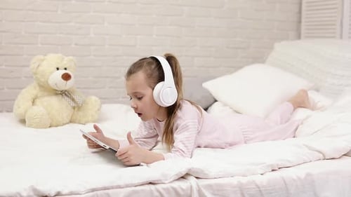 Child Using Tablet with Headphones Lying on Bed