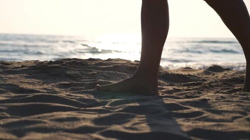 Close Up of Female Feet Walking on Golden Sand at the Beach with Ocean Waves at Background