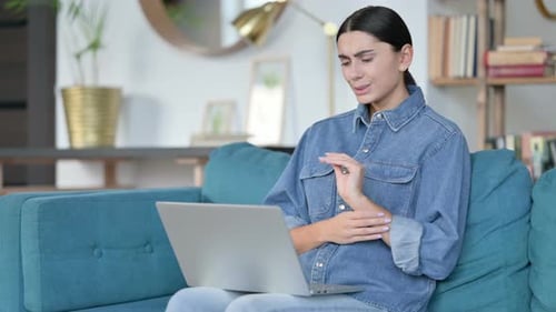 Young Woman Massages Sore Wrist While Using Laptop