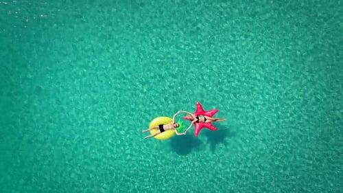 Vista aérea de homem e mulher flutuando em colchões infláveis de mãos dadas.