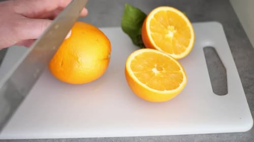 Male Hand Cuts an Orange in Half with a Knife on a Cutting Board