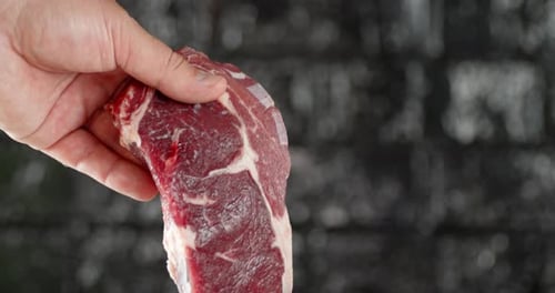 Hand Holding a Raw Steak in Close Up