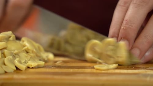 Close view slicing mushrooms on cutting wooden board.