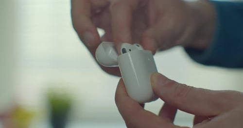 Hands of Young Man Take the Wireless Earphones From the White Case. Close Up