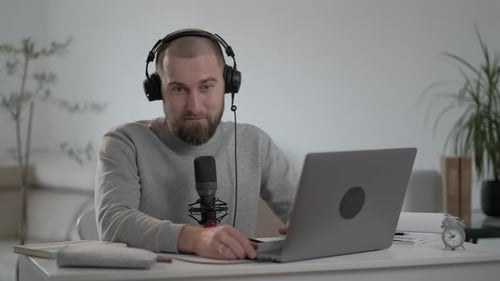 Jovem hippie gravando podcast usando laptop, transmitindo uma entrevista em casa