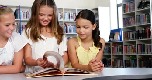 School kids reading book together in library