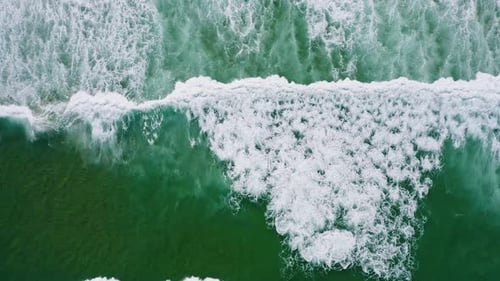 Aerial Top Down Footage of White Waves and Emerald Green Ocean Water Surface Near Sandy Beach