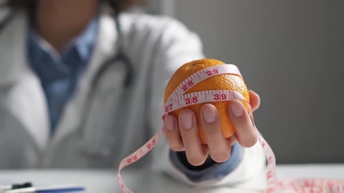 The Nutritionist's Hand Holds An Orange Orange Fruit. Nutritionist Doctor With Food Intake Shows