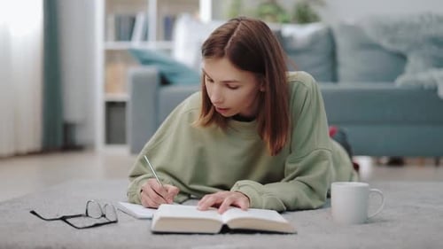 Young Woman Studies While Lying on Rug Indoors