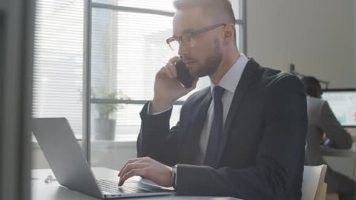 Businessman Talking on Phone and Using Laptop in Office