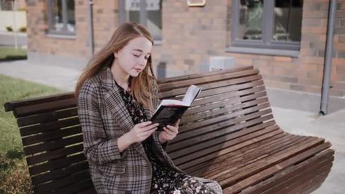 a girl reads a book on a street bench