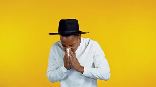 Young Man Sneezing Into a Tissue on Yellow Background