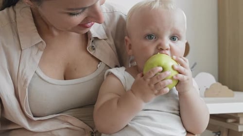 Loving Mother Watches Child Eat an Apple