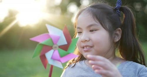 Funny asian girl with colored windmill in the garden