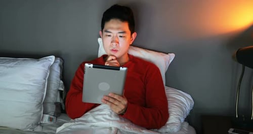 Man Relaxing in Bed with Tablet at Night