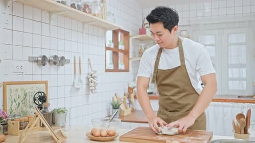 Handsome male kneads yeast dough with his hands, learn how to make bread by looking at tablet.